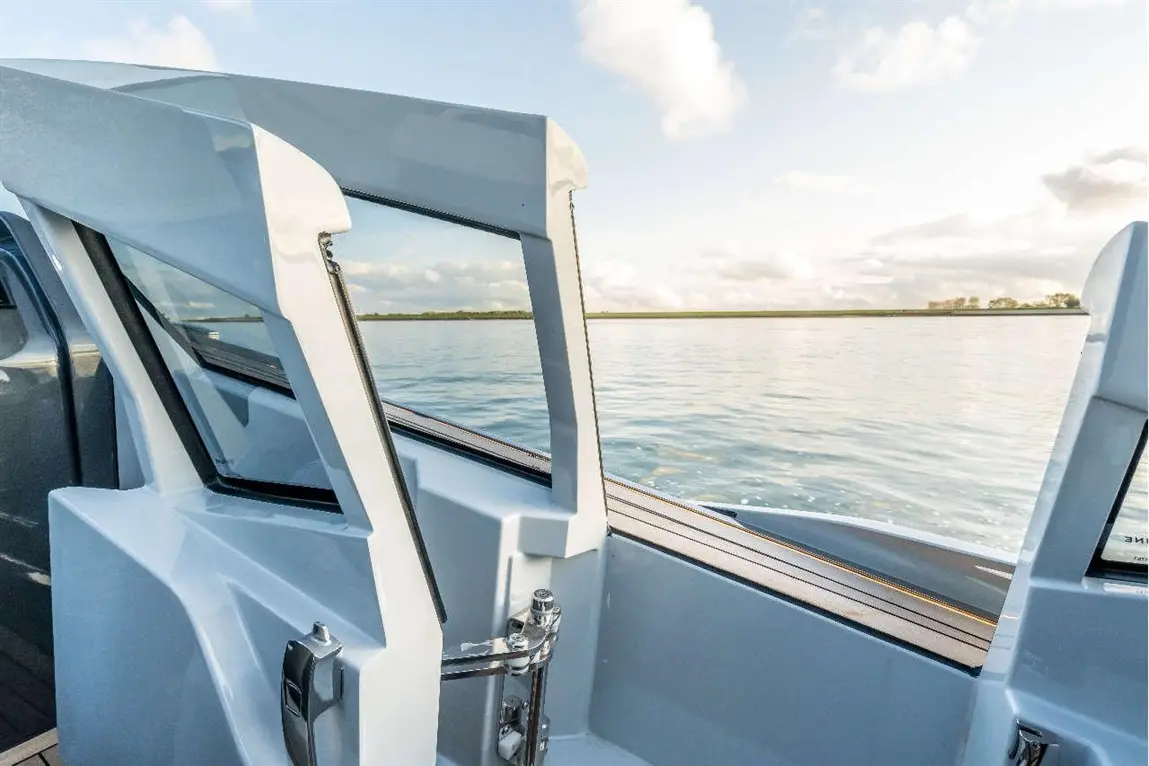 Modern yacht interior with open windows, showcasing calm water and a distant shoreline under a bright sky.